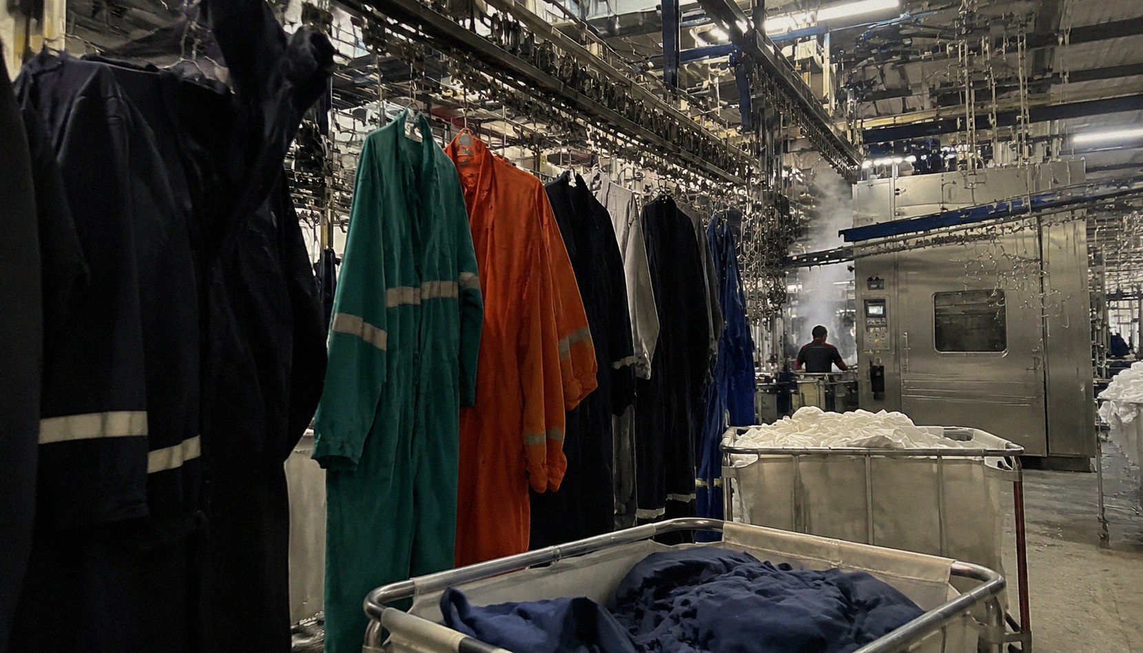 Rows of workwear garments on an overhead conveyor inside a large industrial laundry facility.